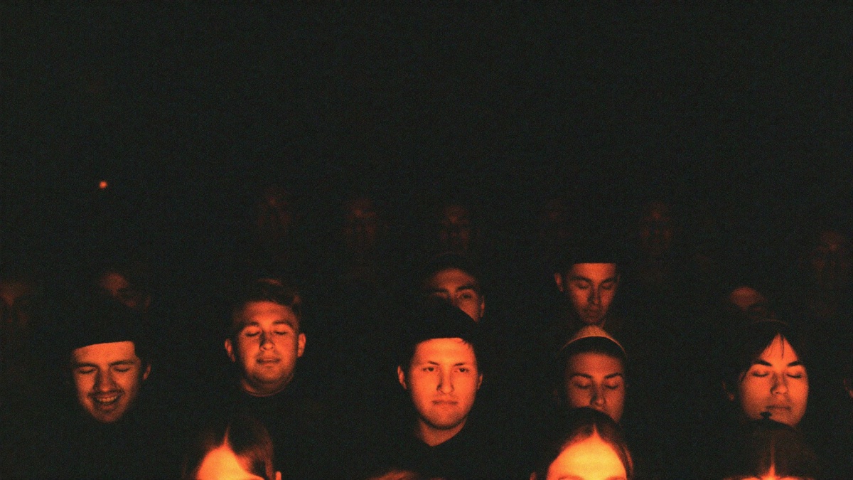 Faces in a crowd singing with eyes closed, lit from below by warm firelight