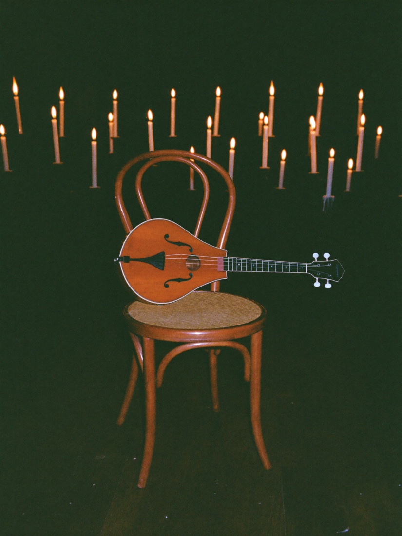 A mandolin resting on an empty bentwood chair, candle flames glowing out of focus behind it